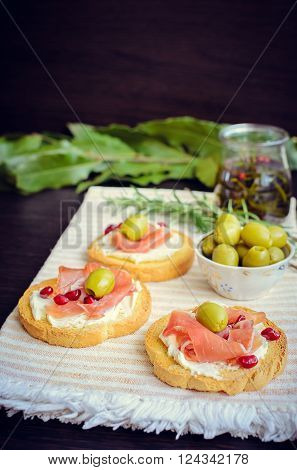 Delicious bruschetta with prosciutto olives and pomegranate on background of olive oil with spices. Italian bruschetta sandwich. Close Up. Italian appetizer. Selective focus.
