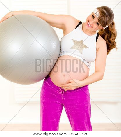 Donna incinta bella sorridente tenendo palla fitness e toccare la sua pancia a soggiorno