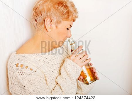 Elderly sad woman sitting in the corner and drinking whiskey