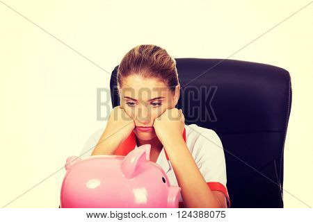 Female doctor sitting behind the desk and holding a piggybank
