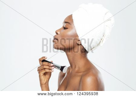 Side view portrait of afro american woman applying makeup with brush isolated on a white background