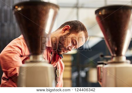 Caucasian man working in a coffee roastery, concentrating on his work behind two modern coffee ginders