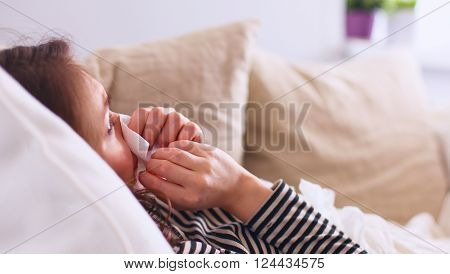 Portrait of a sick woman blowing her nose while sitting on the sofa.
