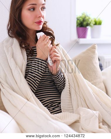Portrait of a sick woman blowing her nose while sitting on the sofa.