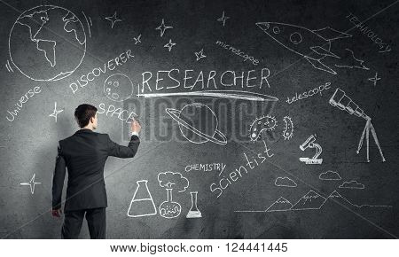 Rear view of man drawing education concept on blackboard with chalk