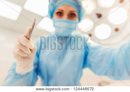 Beautiful female surgeon is holding a scalpel ready to operate and looking at camera standing in a modern operating room bottom view