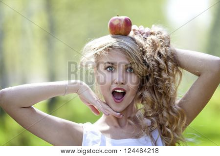 Beautiful young girl with long hair is holding a green apple on her head