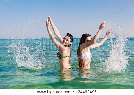 Two beautiful young girls in bathing suits and sunglasses fun squirting into the sea on a hot day