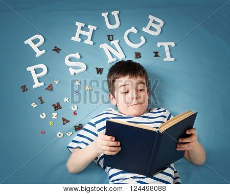 seven years old child lying with book and letters on blue background