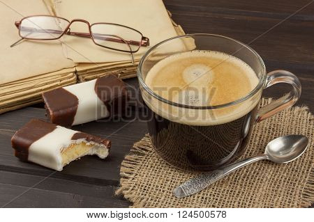 Old books, eyewear and cup of coffee on a dark wooden table. Reading vintage old book and coffee. Relax with a book and a good coffee.