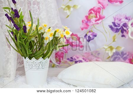 Bouquet of daffodils in a white vase with white cushions in the interior
