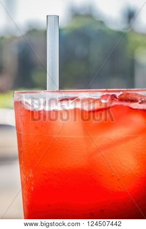 Red cordial drink in a cup, with ice and straw. Focus is generally on the straw.
