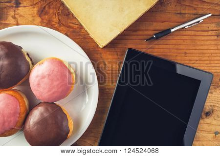 Delicious donuts and digital tablet computer on the table top view of homemade tasty doughnuts old book and electronics gadget.