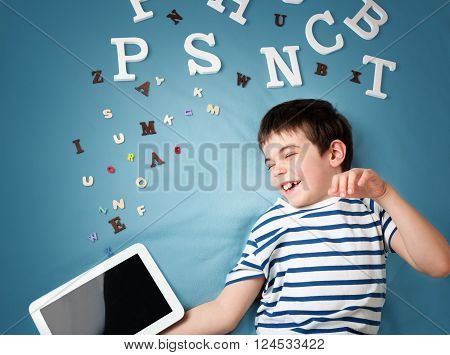 seven years old child lying with tablet and letters on blue background