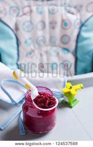 Baby food from beets on the table against the background of toys. Selective focus.
** Note: Shallow depth of field