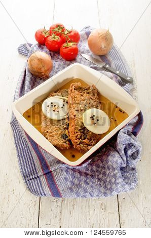 fried herringfilet with onion pepper and mustard seeds in a bowl fresh tomato and kitchenknife in the background