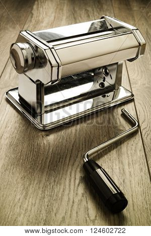 Metal reflective pasta machine with separated hand crank wood surface. Selective focus on pasta machine.