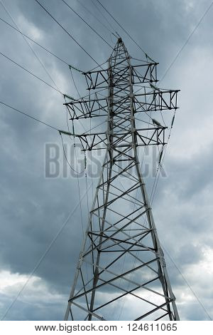 Electric pole power lines and wires on storm omnious sky. High voltage electricity pylons against rainy cloud.