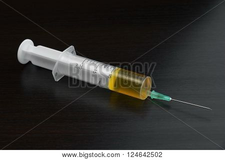 Single Syringe With Yellow Liquid On The Black Wood  Background