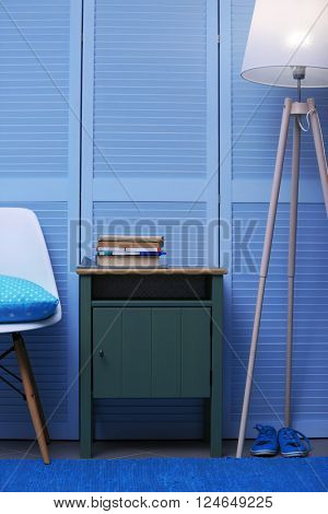 Small green table with books and lamp near blue wooden wardrobe