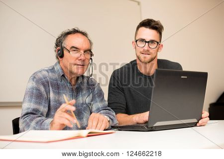 Young man teaching eldery man of usage of computer. Intergenerational transfer of computer skills.