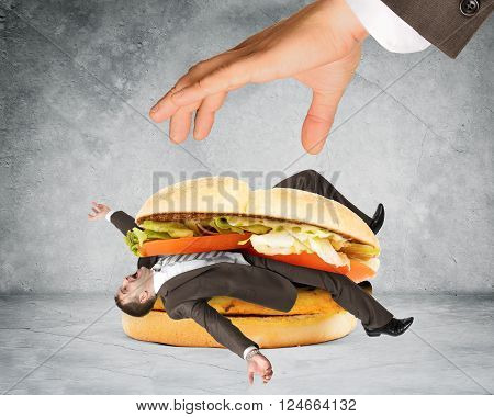 Businessman inside hamburger and big humand hand on grey wall background