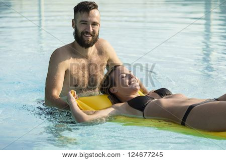 Young handsome man pulling his girlfriend through the swimming pool on an airbed