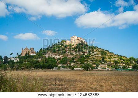 Pilgrimage church of Sant Salvador on green hill in Arta village, Mallorca island, Spain. Beautiful landsacape with medieval architecture, green trees and blue sky with clouds on a sunny day.
