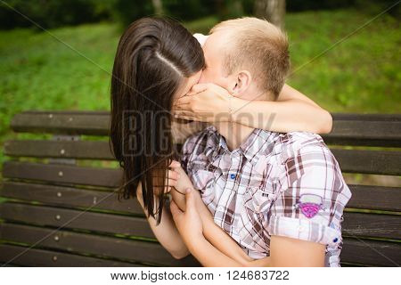 Portrait of attractive young girl kissing her boyfriend and closing their lips by hand in park