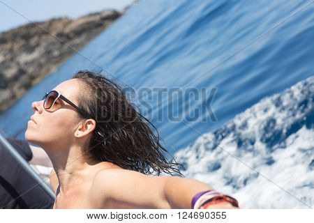 Calm young woman with eyes closed taking sunbath while leaning on shipboard against of blue water. Copy space area