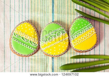Easter homemade gingerbread cookie and yellow end green eggs over grenn and white cloth. Colorful image top view