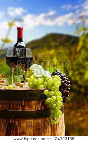 Red wine bottle and wine glass on wodden barrel. Beautiful Tuscany background