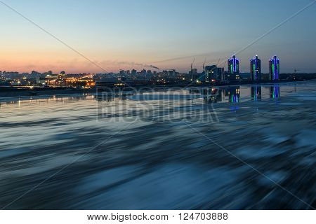 Scenic night view on the breaking of the ice on the river with a fast flowing on the background of city with lights and reflections in water shot on a long exposure