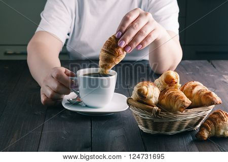 woman dipping croissant in cup of coffee