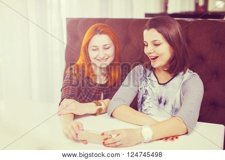 Group of friends having fun at the cafe and looking at smart phone. Man showing something to his friends sitting by, focus on mobile phone.