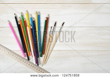 Layout of set of colorful sharp pencils, a centimeter rule and paint brushes on a wooden blank board. Art composition.
