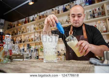 barman using a hand mixer to prepare drink in  bar or pub