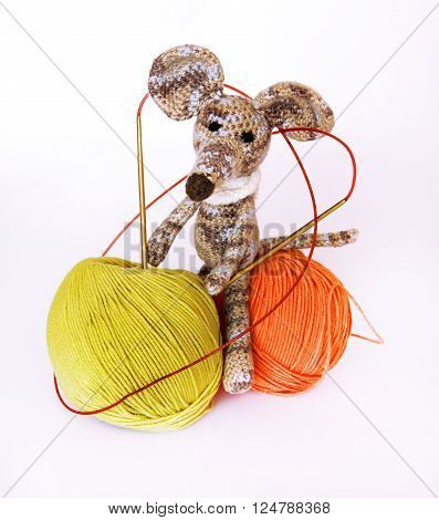 small colorful knitted toy mouse in a white scarf playing with colored yarn threads of wool Bright children's toy clew