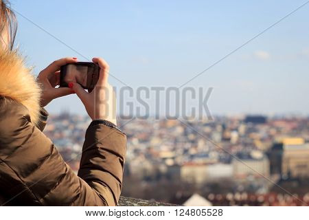 Pretty young girl taking / shooting a picture / video of big history city during the winter sunset (color toned image)