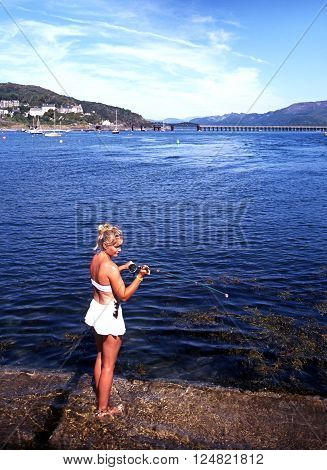 BARMOUTH, UK - AUGUST 6, 1995 - Woman fishing from the quay with views towards the railway bridge Barmouth Gwyedd Wales UK Western Europe, August 6, 1995.