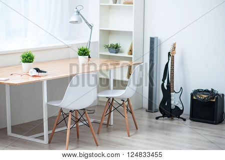 Music world.  View of a nice specious room with big table standing near the window and the guitar standing on the floor