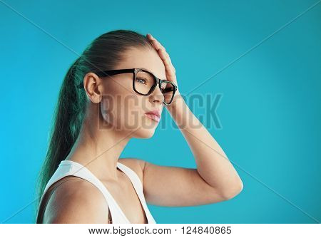 Portrait of young sick female suffering from migraine or vertigo over blue background. Concept of head illness diagnosis and treatment.