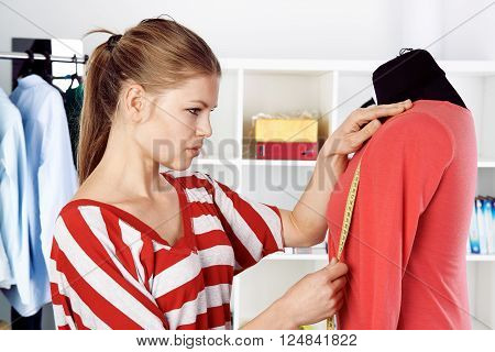 Young female dress stylist measuring clothing on model for making seam. Woman atelier owner sewing in studio.