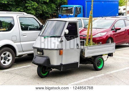 OVADA, FRANCE - AUGUST 7, 2014: Grey three-wheeled light commercial vehicle Piaggio Ape in the city street.