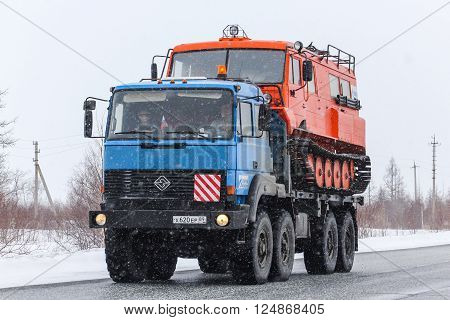 NOVYY URENGOY, RUSSIA - APRIL 16, 2013: Blue off-road truck URAL 5323 carries the all-terrain vehicle TTM-3902 Taiga at the interurban road during a snowfall.