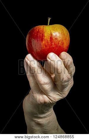 Old hand holding an apple on black background