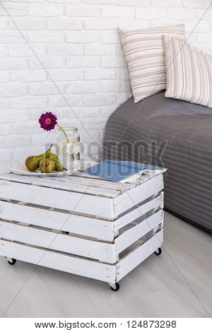 Light bedroom with white brick wall, bed with grey bedding and nightstand made from wood box