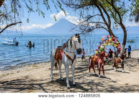 Lake Atitlan Guatemala - April 4 2016: Local families relax on shores of Lake Atitlan with San Pedro volcano behind. Parents pay for children to sit on life size model horses.