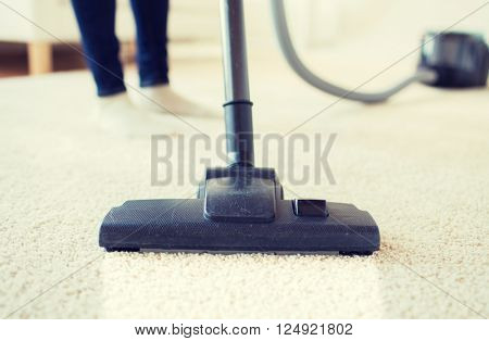 people, housework and housekeeping concept - close up of woman with legs vacuum cleaner cleaning carpet at home