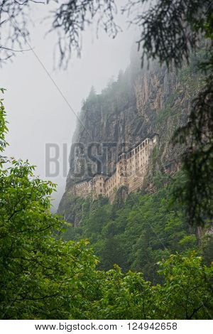 Sumela monastery in the cliff with bright green trees in foreground.